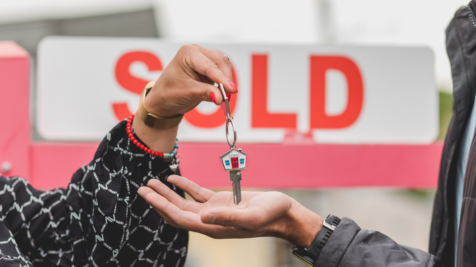 Handshake between two individuals in front of a house with a sold sign, symbolising a peaceful property buyout and new beginnings.
