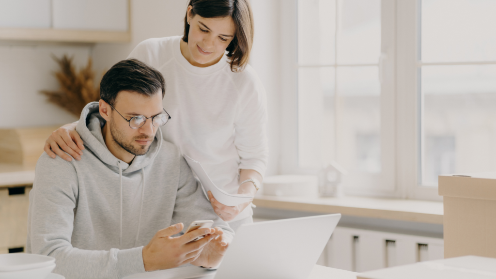 Young couple researching about mortgages, surrounded by documents and a model house, symbolizing first-time home buying.